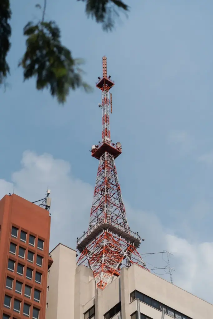 Close-up of a red and white television antenna atop a city building under a clear blue sky.