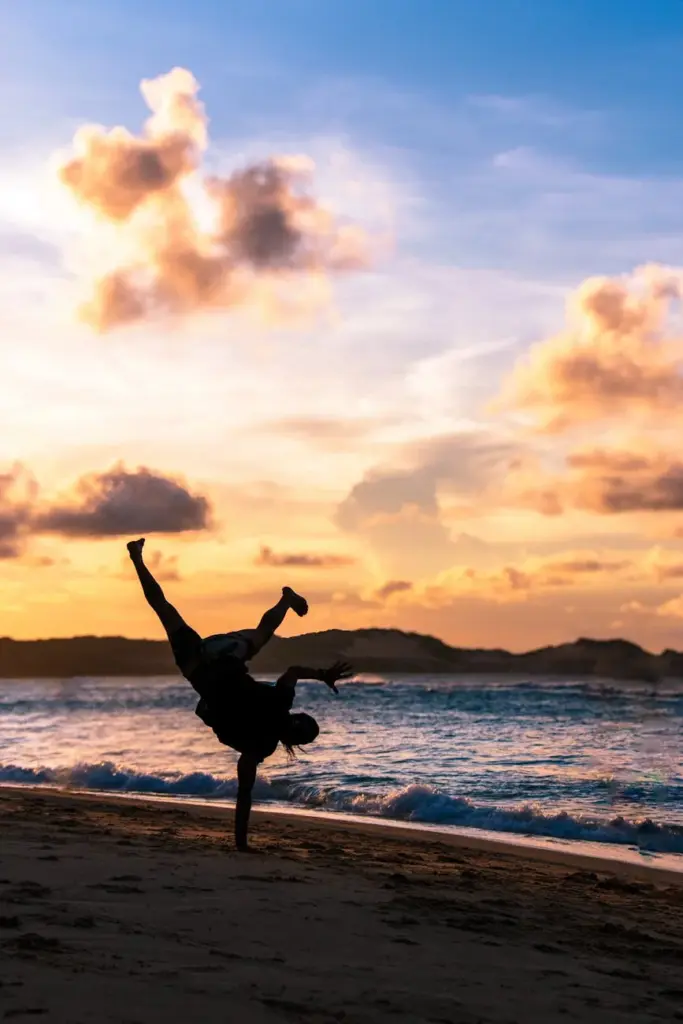 A person performs a handstand on the beach at sunset, creating a stunning silhouette against the vibrant sky at Pipa Beach, Brazil.