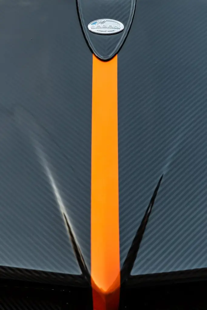 Detailed shot of a high-end sports car hood with carbon fiber texture and orange stripe.