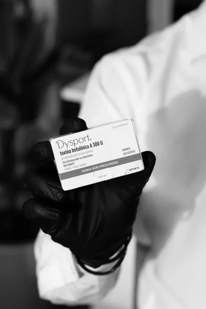 Black and white image of a gloved hand holding a Dysport botulinum toxin box, indicating medical or cosmetic use.