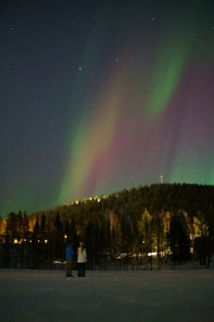 Breathtaking view of the Northern Lights over snowy Lapland, Finland, with two people gazing at the vibrant aurora.