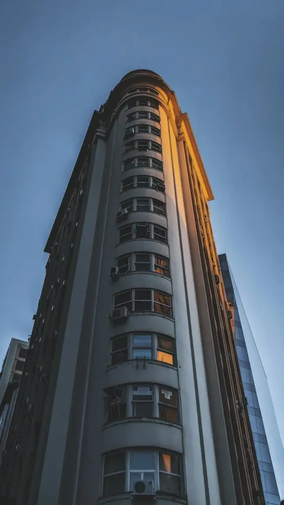 From below exterior of contemporary high residential building with triangle flatiron shaped design located on city street against blue sky