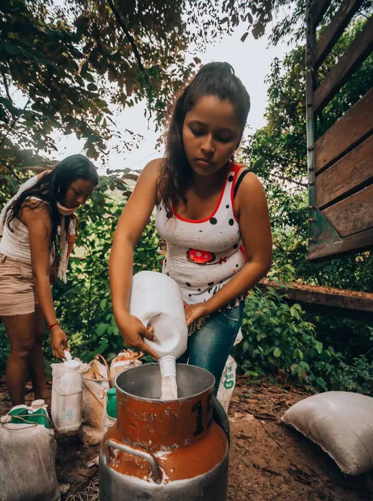 Young woman pouring milk into a container in a countryside setting, showcasing rural life.