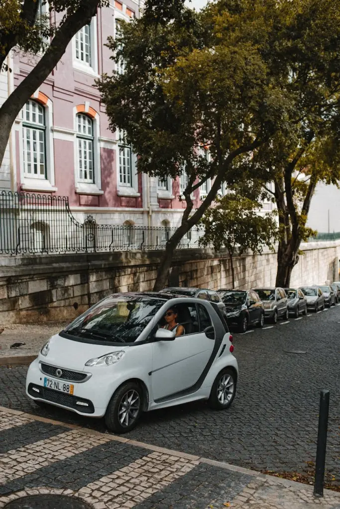 A small electric smart car parked on a cobblestone street in Lisbon, Portugal, near historic architecture.