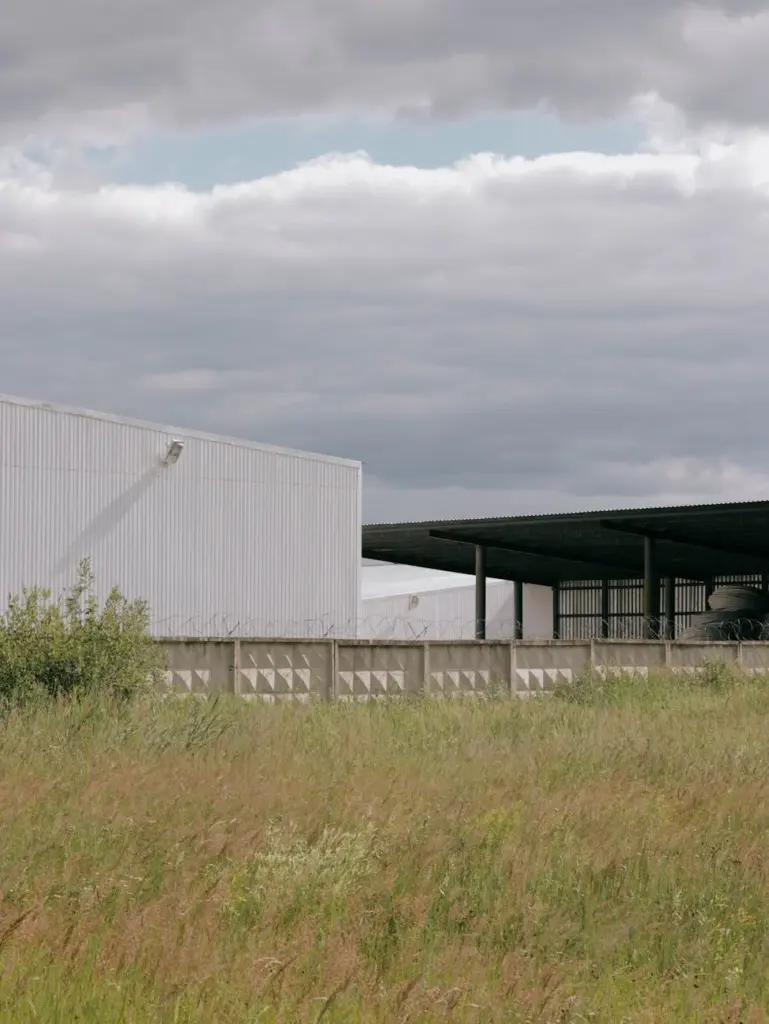 White industrial building backdrop against a grass field and overcast sky.