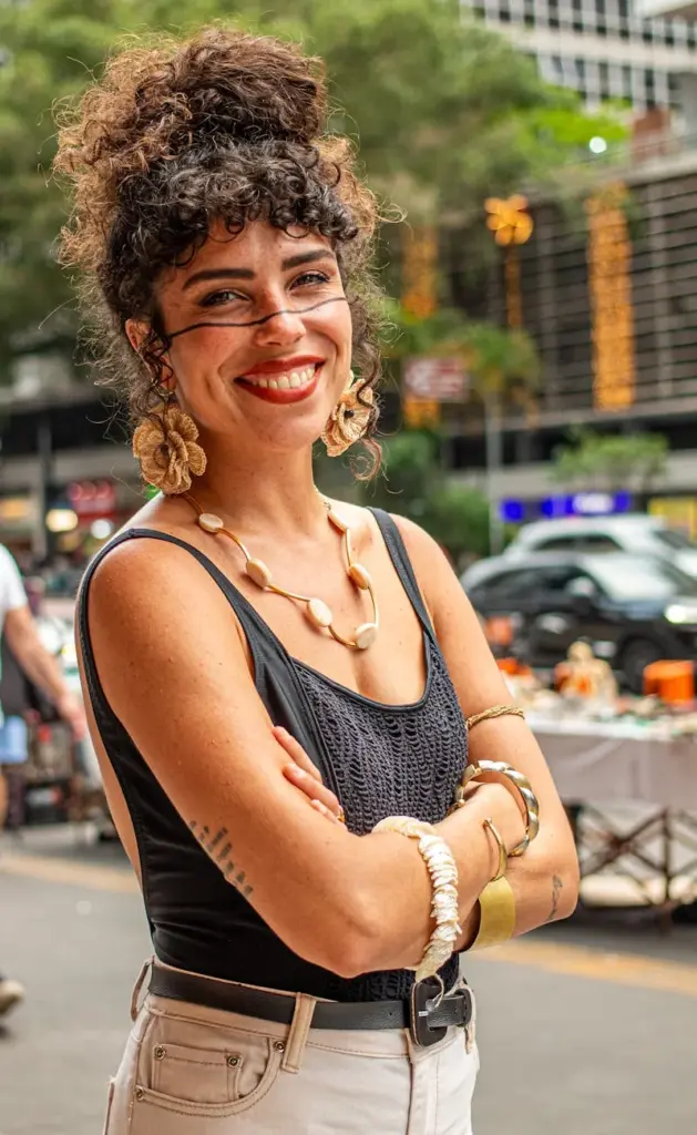 Confident woman with earrings smiling at an outdoor market in the city.