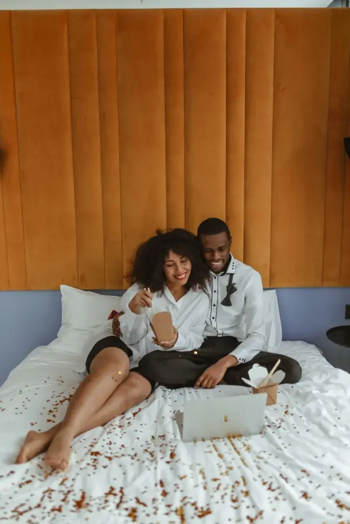 Happy couple sitting on bed with laptop, enjoying a relaxed moment at home.