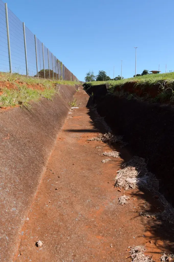 Concrete canal beside a metal fence under a clear blue sky in Brasília, Brazil.