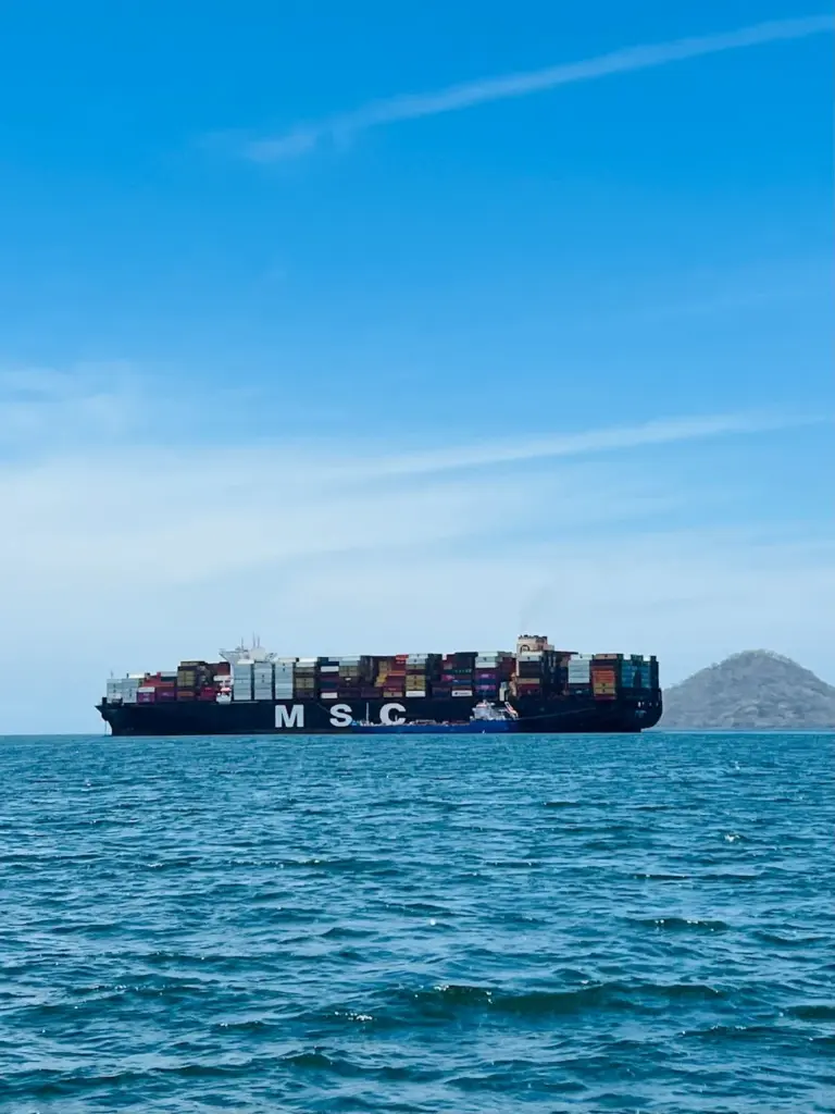 Large cargo ship carrying containers on a calm ocean with a clear blue sky.