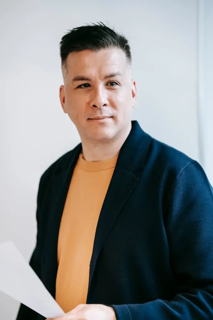 Portrait of a confident adult man in a blazer, holding paper, showcasing professional and stylish attire.