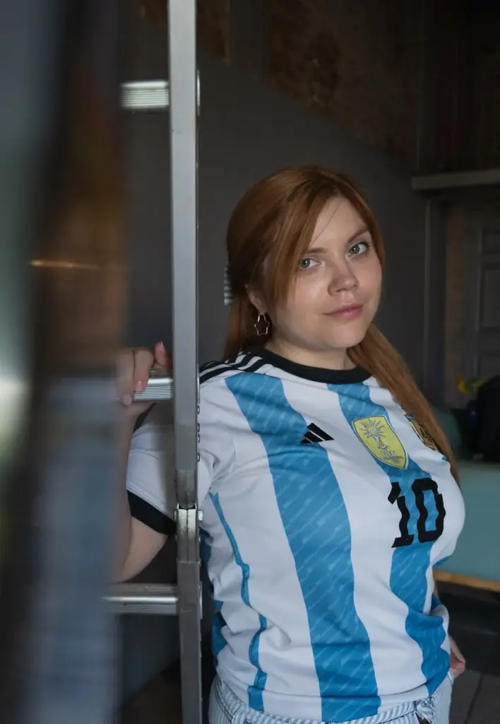 Portrait of a young woman wearing an Argentina soccer jersey indoors, looking confident.