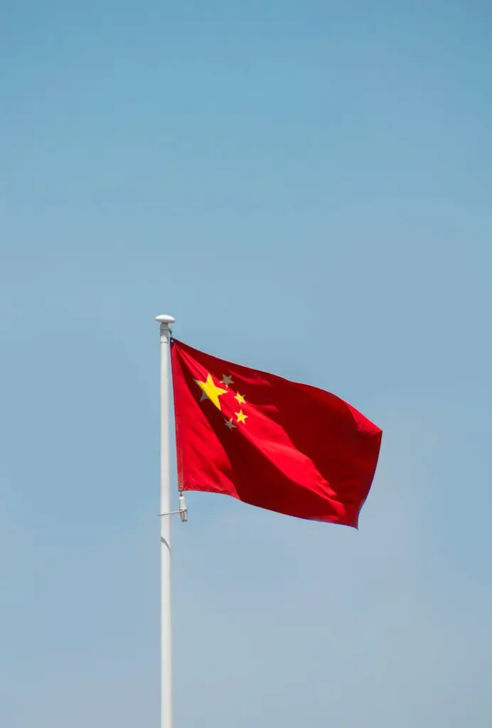 A minimalist photo of the Chinese flag waving on a flagpole against a bright blue sky in Beijing.