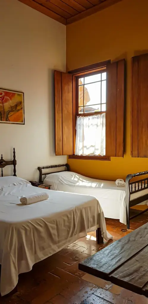 Cozy rustic bedroom in Brazil with sunlight streaming through wooden shutters.