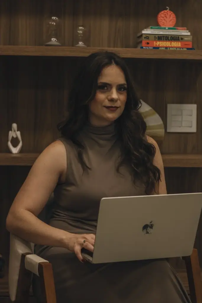 Confident woman sitting in an office with a laptop, surrounded by books.