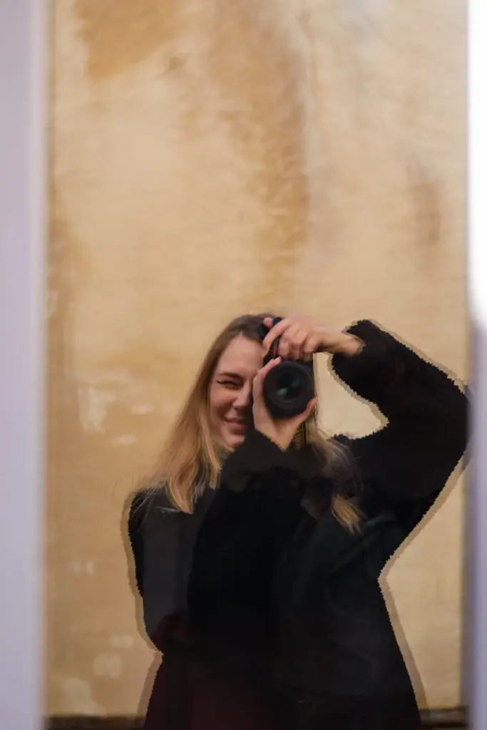 A woman holding a camera appears through a glass reflection, capturing her focused expression.