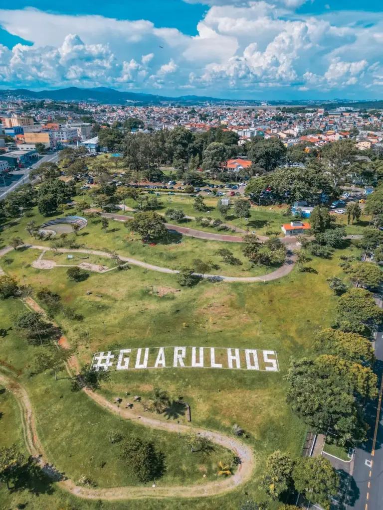 Drone shot of Guarulhos park with cityscape and greenery on a sunny day.