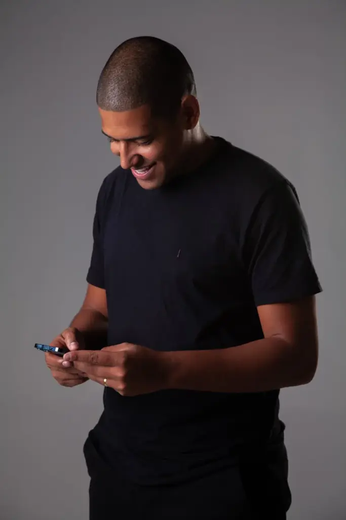 Smiling man in a black shirt using a mobile phone in a studio setting.