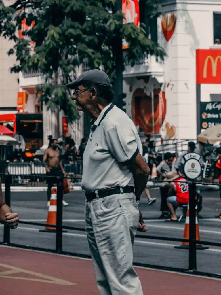 Senior man standing on a busy street, city life scene with vibrant urban elements.