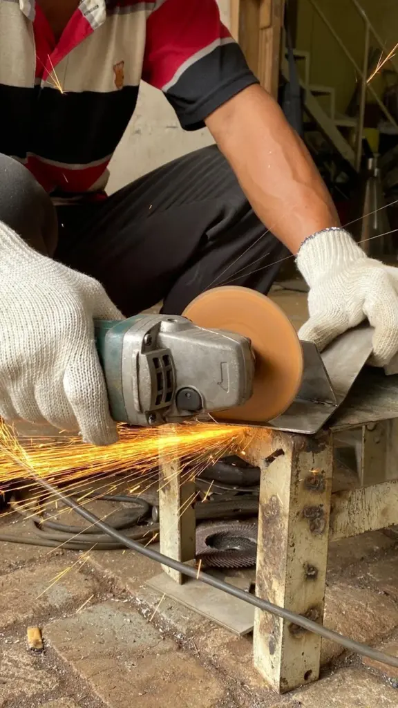 Crop anonymous male worker in gloves cutting metal detail with grinder with sparks while working in workshop