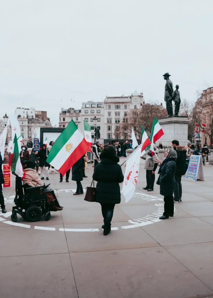 A group of protesters gather in Trafalgar Square, London, holding Iranian flags and signs.