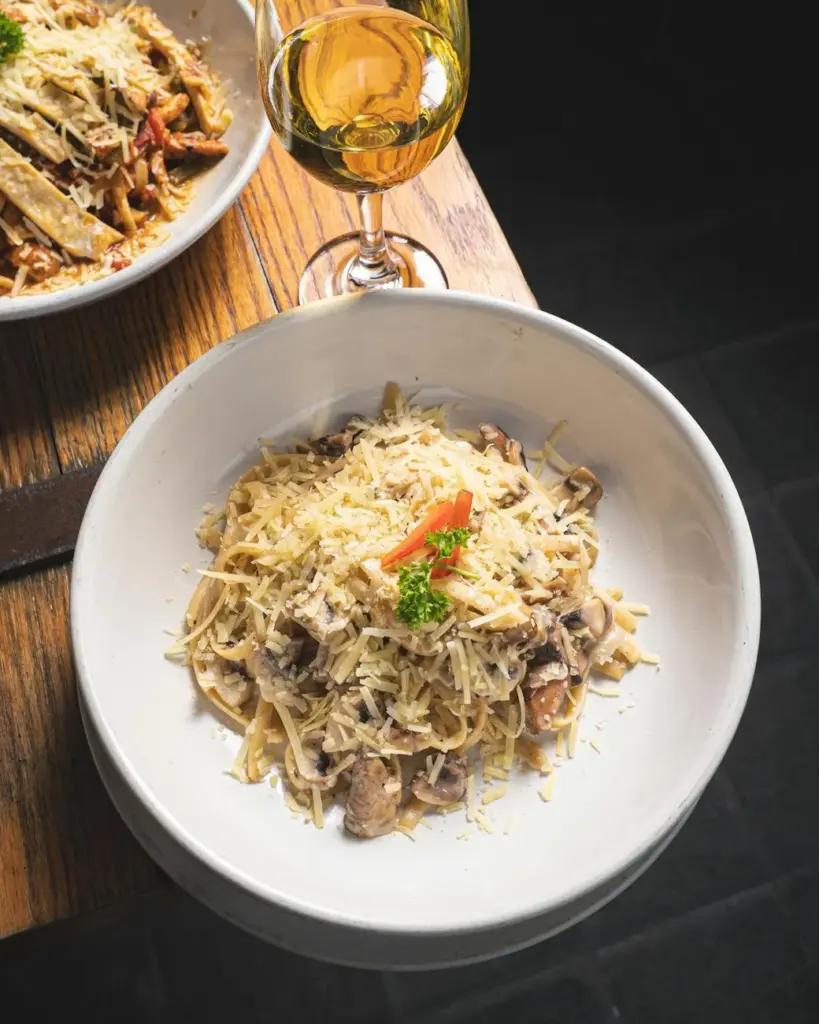Savor a classic Italian pasta garnished with cheese and paired with a glass of white wine.