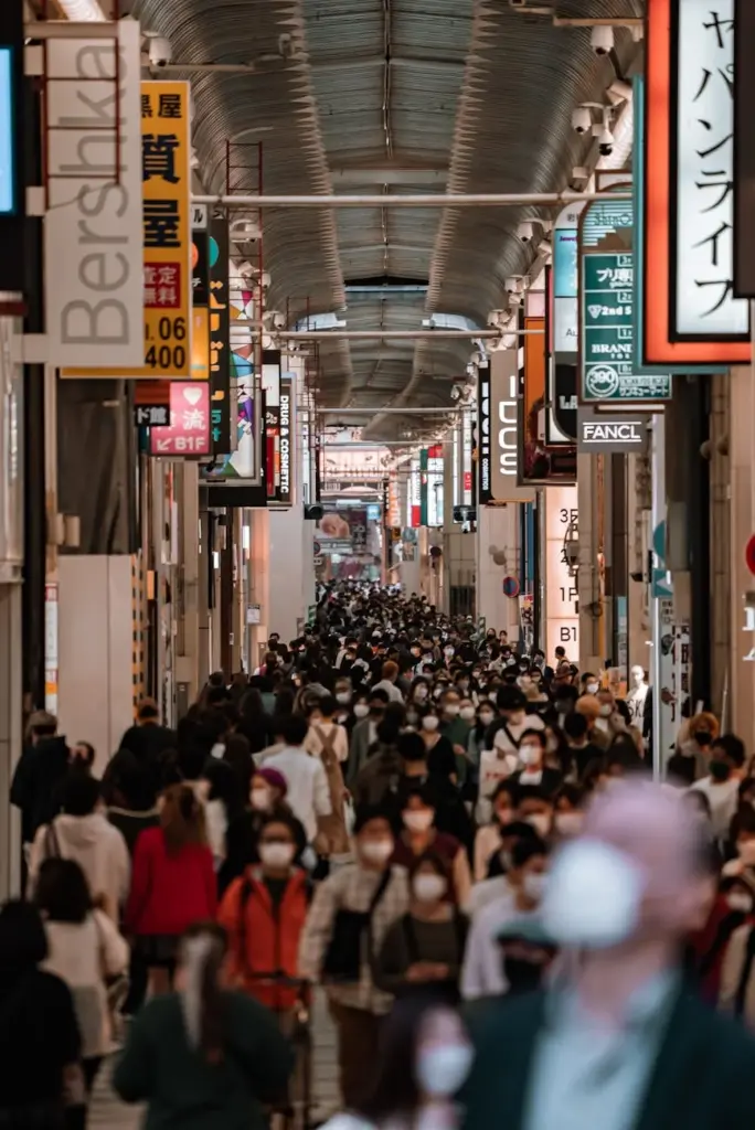 Crowds walk under neon lights in a vibrant Osaka shopping arcade, capturing the urban energy.