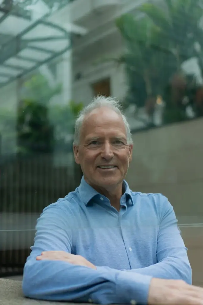 Elderly man smiling inside a modern glass architecture with greenery.