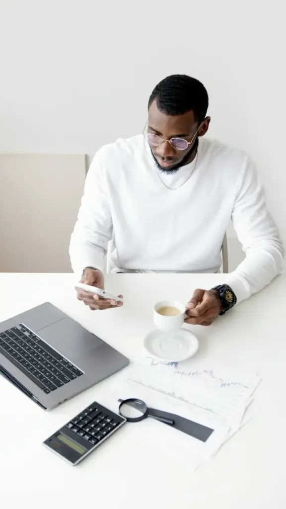 A professional man multitasking with a smartphone and coffee in an office setting.