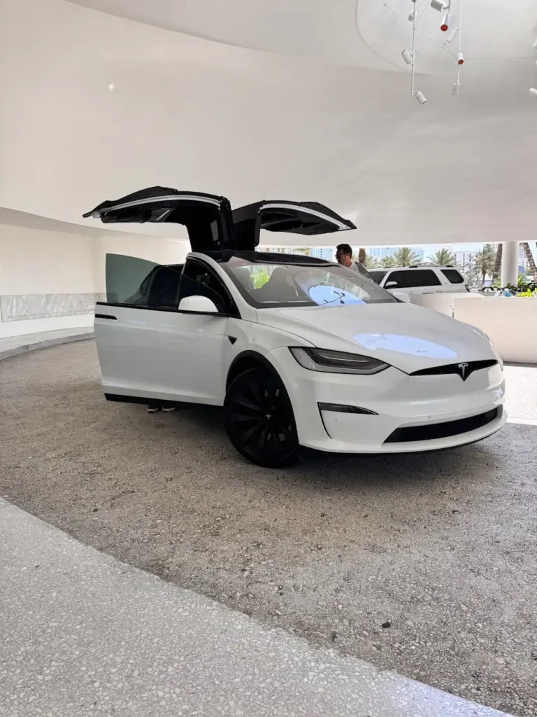 A modern white electric car with falcon wing doors open in an indoor setting.