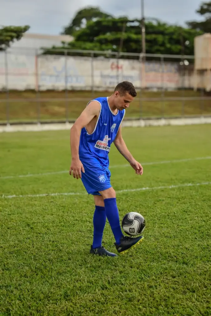 A young soccer player in a blue uniform practicing with a soccer ball on an outdoor field.