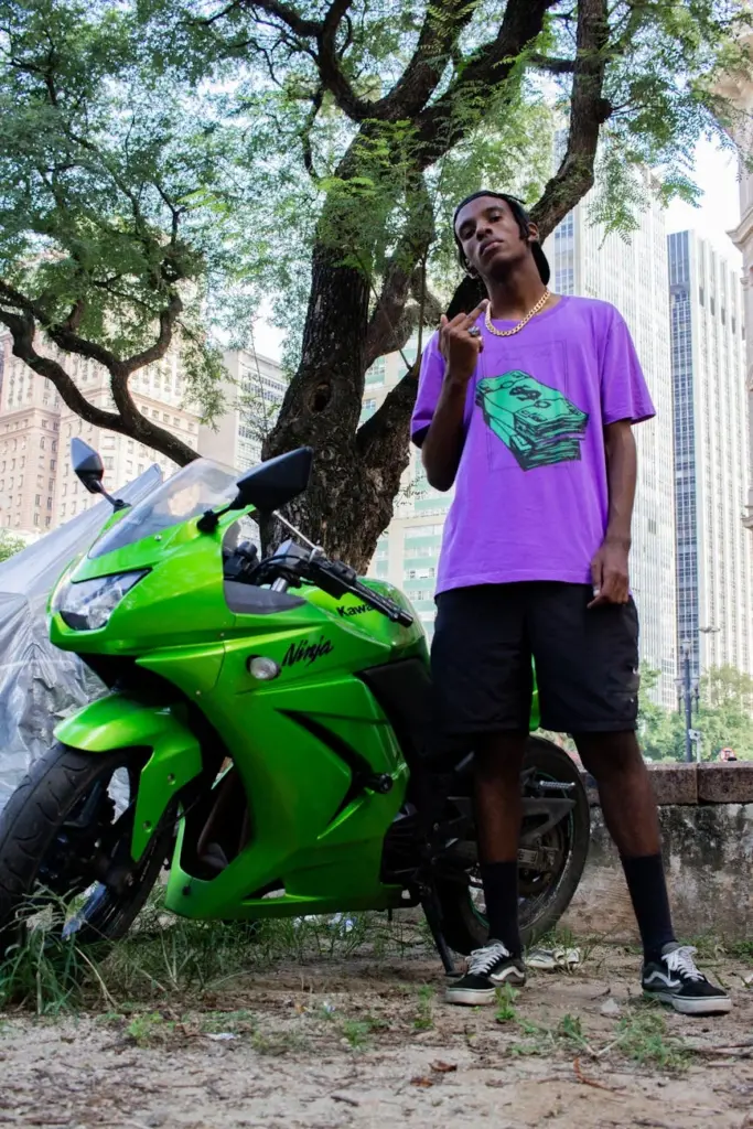 Young man posing with a vibrant green motorcycle in a lively urban area.
