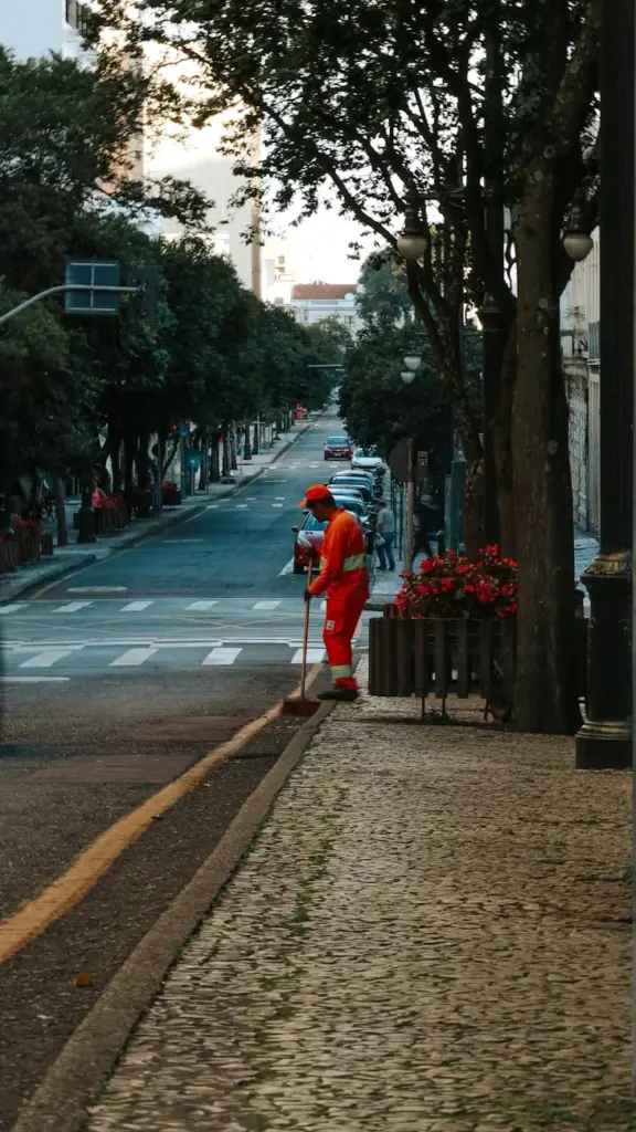 A street cleaner in an orange uniform works on a city road in Curitiba, Brazil, during early evening.