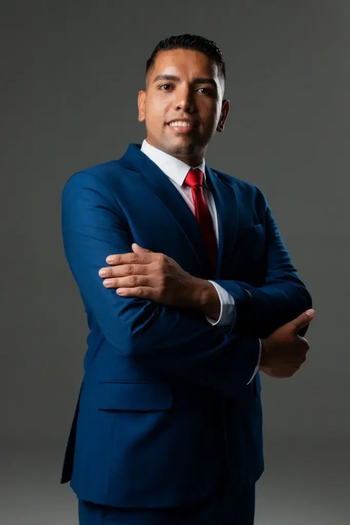 Confident businessman in a blue suit with crossed arms on a gray background.