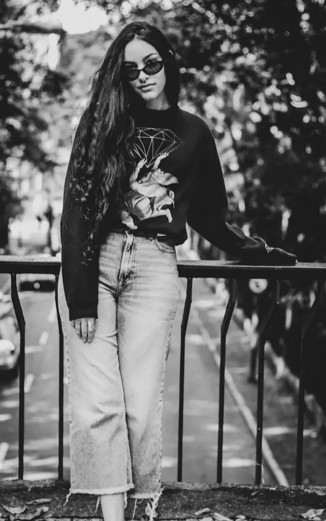 Chic young woman poses casually on a city street in a stylish black and white photograph.