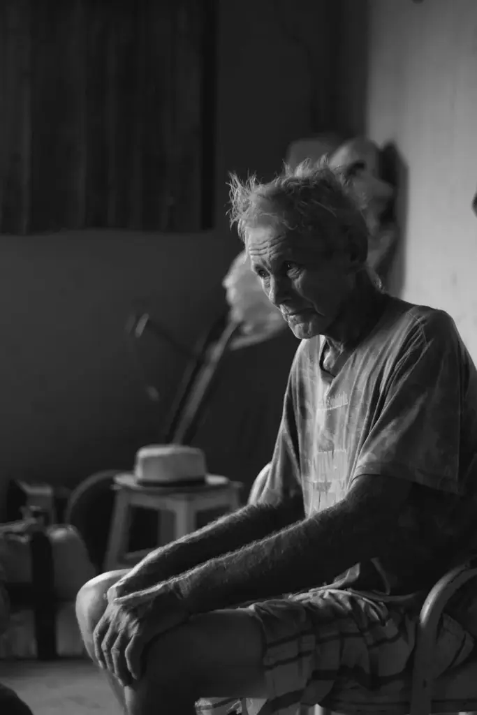 Black and white portrait of a senior man sitting indoors, conveying a reflective mood.