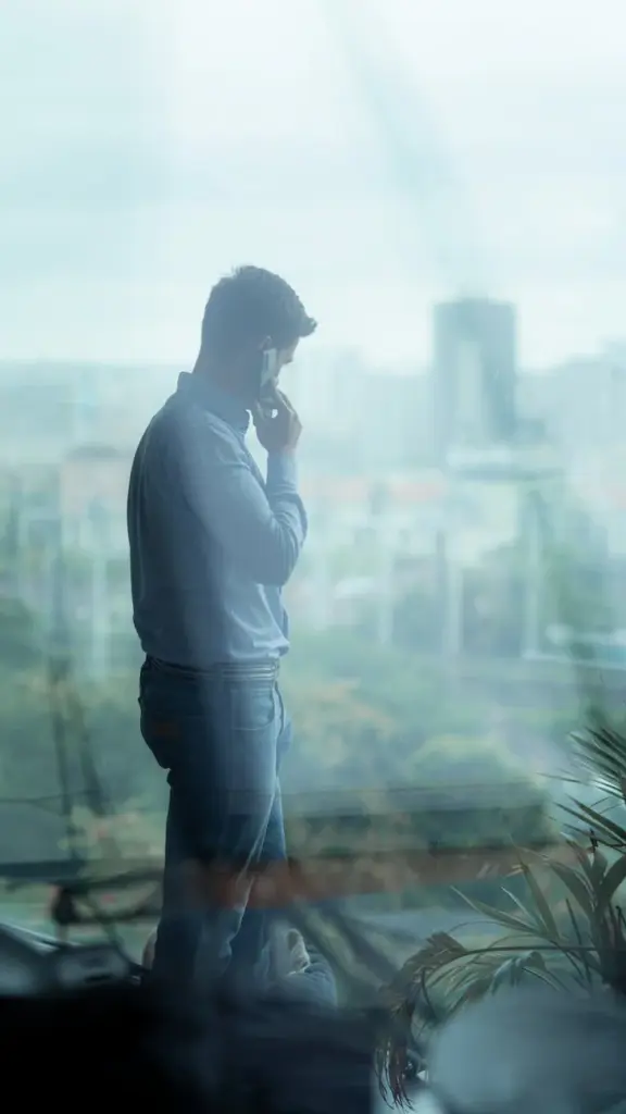 Side profile of a businessman on a phone call inside an office with a cityscape view.