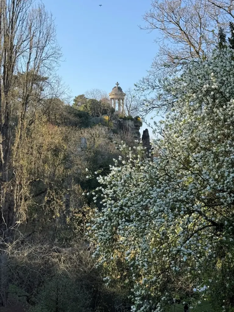 View of Temple de la Sibylle amidst blooming spring foliage in Buttes-Chaumont, Paris.
