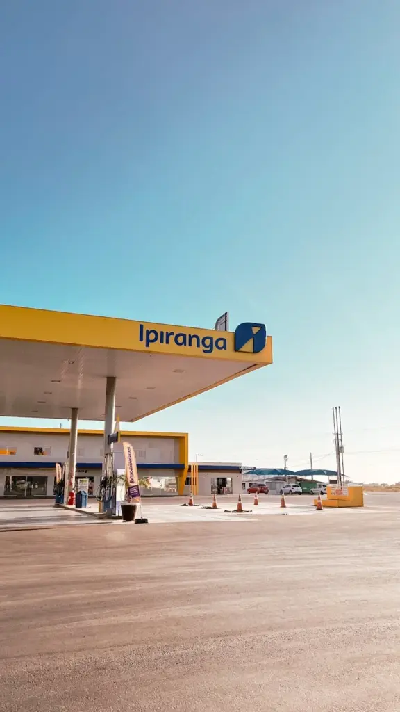 A bright and clean Ipiranga gas station under a blue sky, featuring multiple fuel pumps and open space.