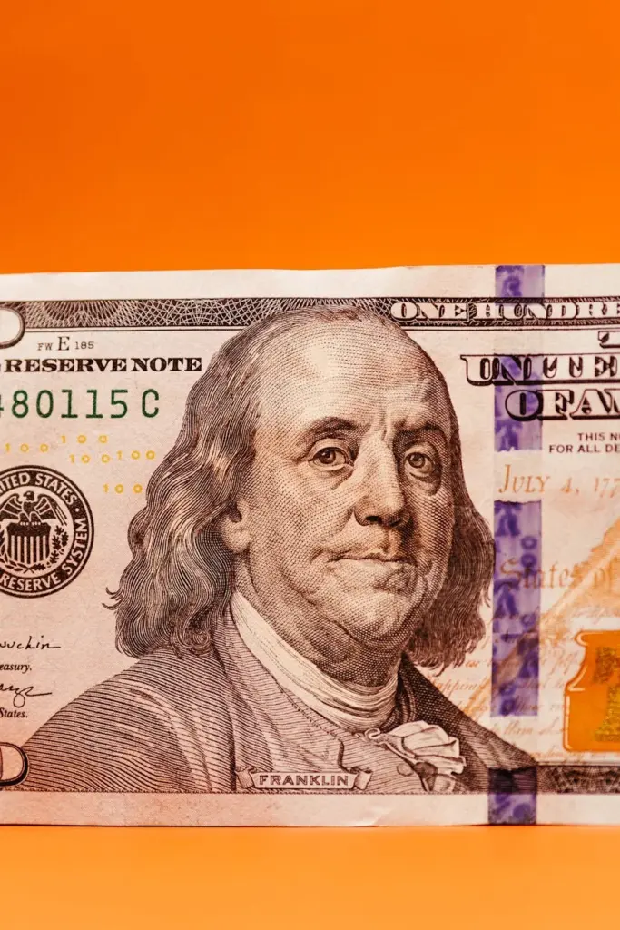 Close-up of a one hundred dollar bill featuring Benjamin Franklin against an orange background.