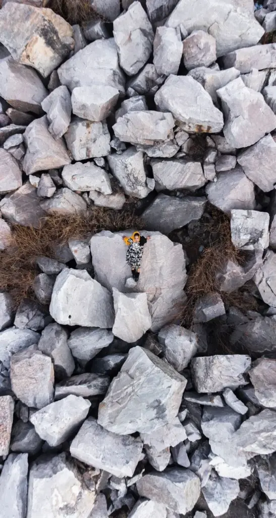 A woman lies in a bold print dress among large rocks in Kaduna, Nigeria, viewed from above.