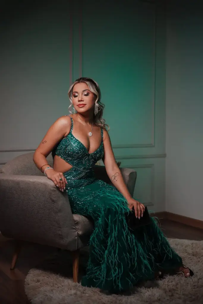 Elegant woman in a sequined green evening gown seated on a chair indoors with soft lighting.