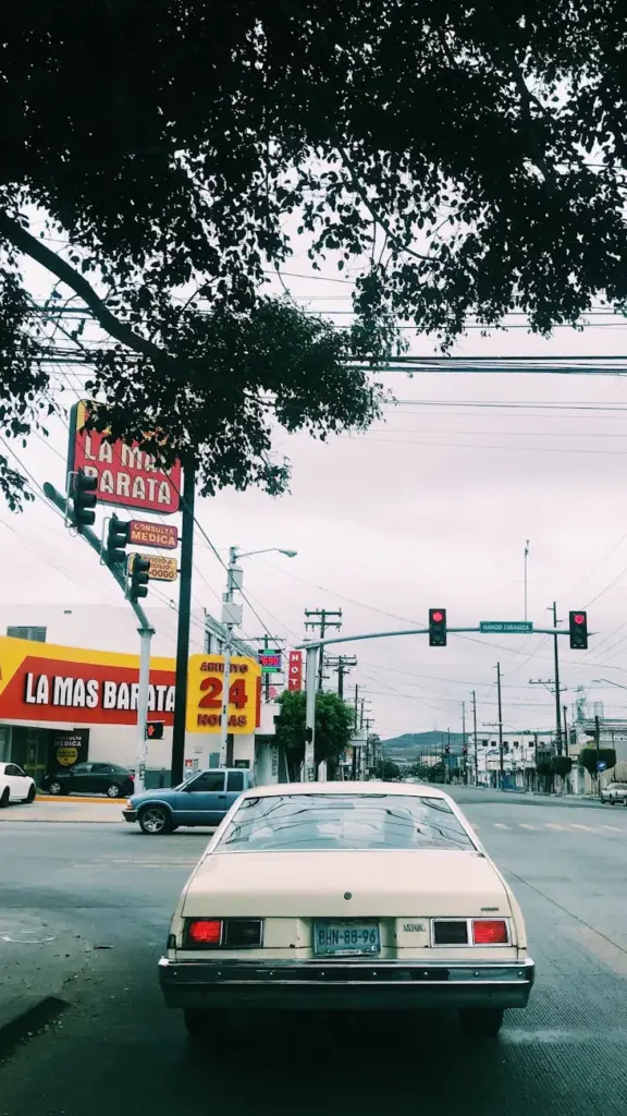 A classic vintage car cruises through the streets of Tijuana, México, under a cloudy sky.