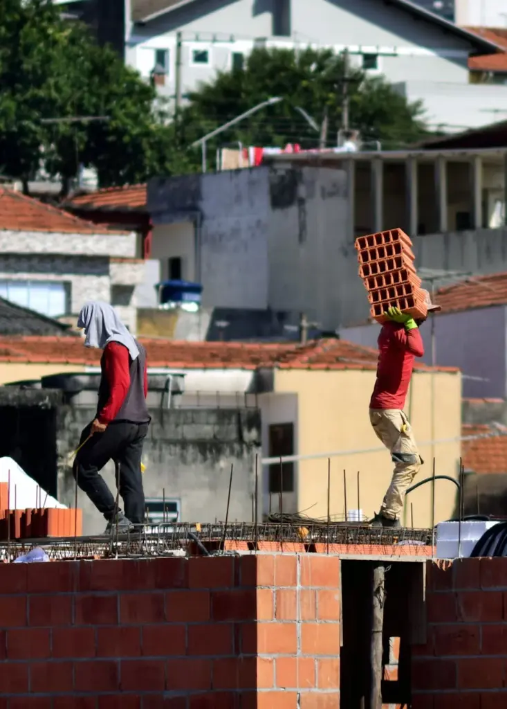 Construction workers carrying bricks on a sunny day in São Paulo, Brazil.