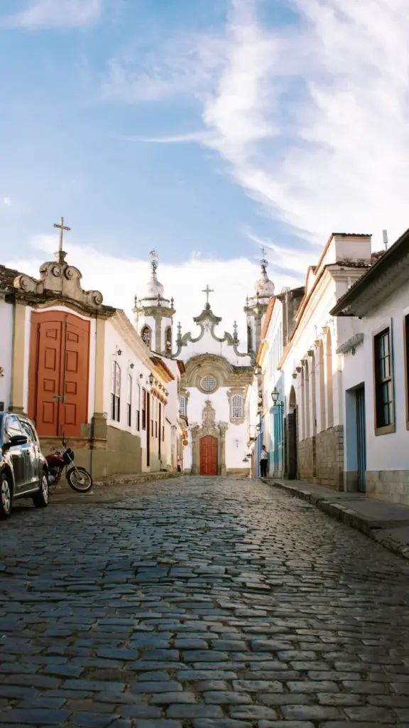Street view of the Nossa Senhora do Carmo Church in São João del Rei, Brazil, with colonial architecture and cobblestone pathway.