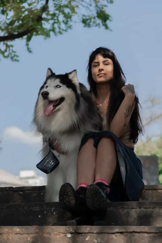 A woman relaxes with her Siberian Husky on outdoor stone steps, enjoying a peaceful moment.
