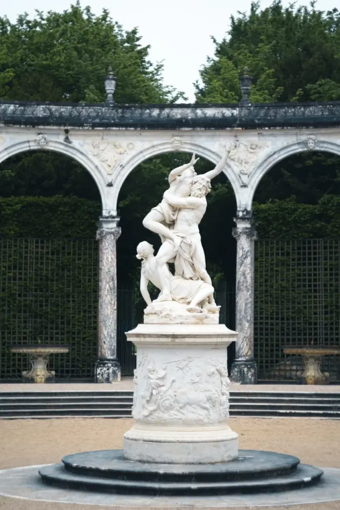 Elegant marble sculpture amidst classical arches in a lush garden setting.