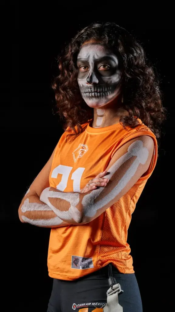 Portrait of a female athlete in skeleton makeup wearing an orange jersey, posing confidently with arms crossed.