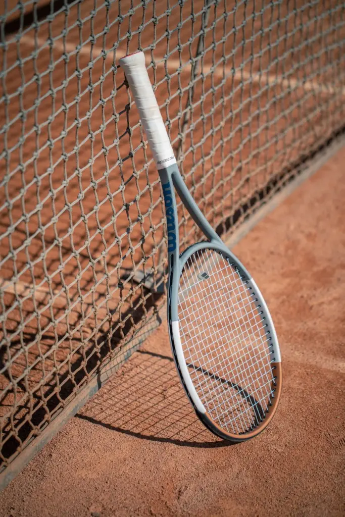 A tennis racket leaning against a net on a sunny clay court, perfect for sports-related themes.