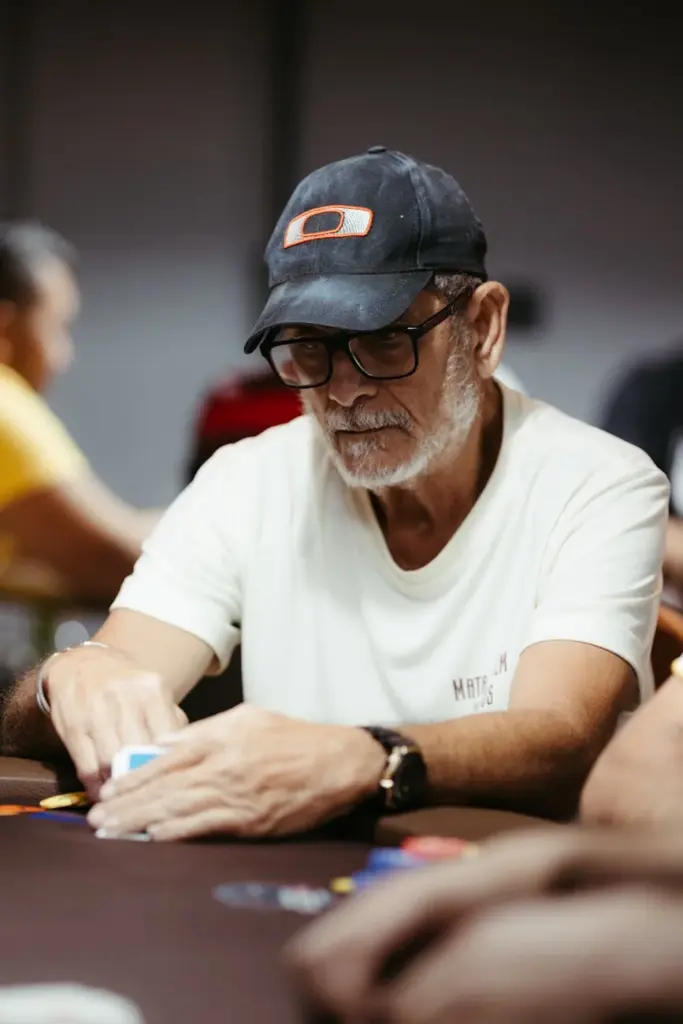 Older man in casual attire focused on a poker game, sitting at a casino table.