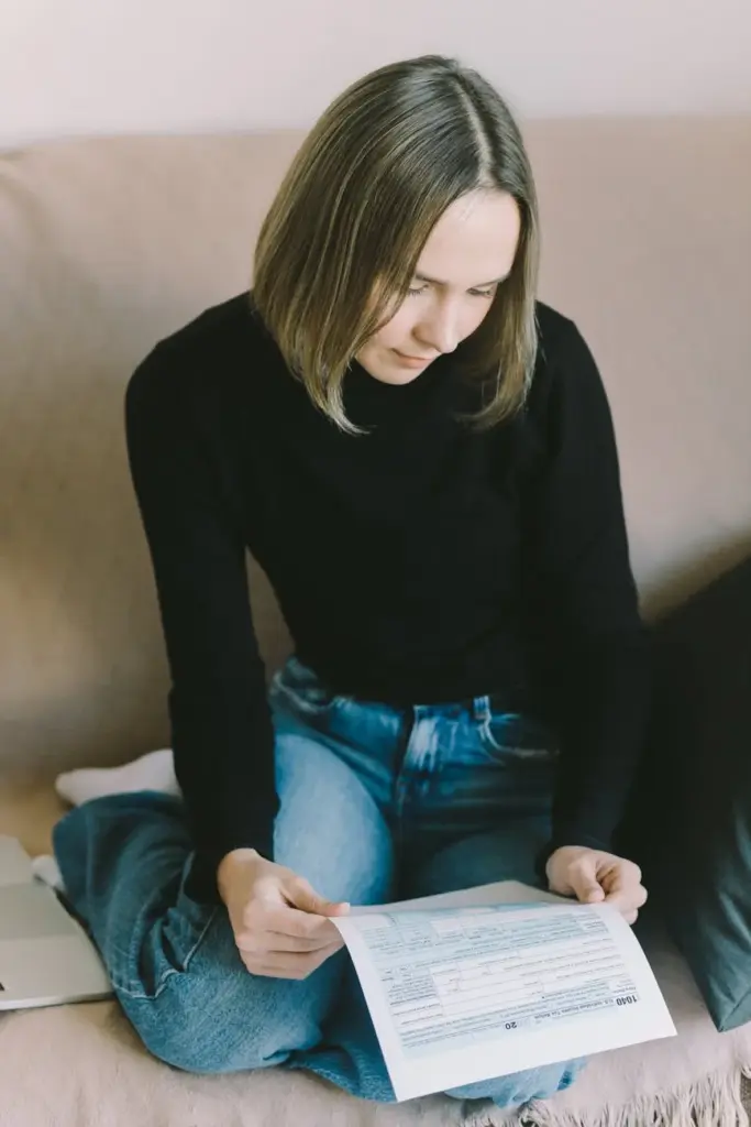 Young woman in black sweater reviewing a document while sitting comfortably indoors.
